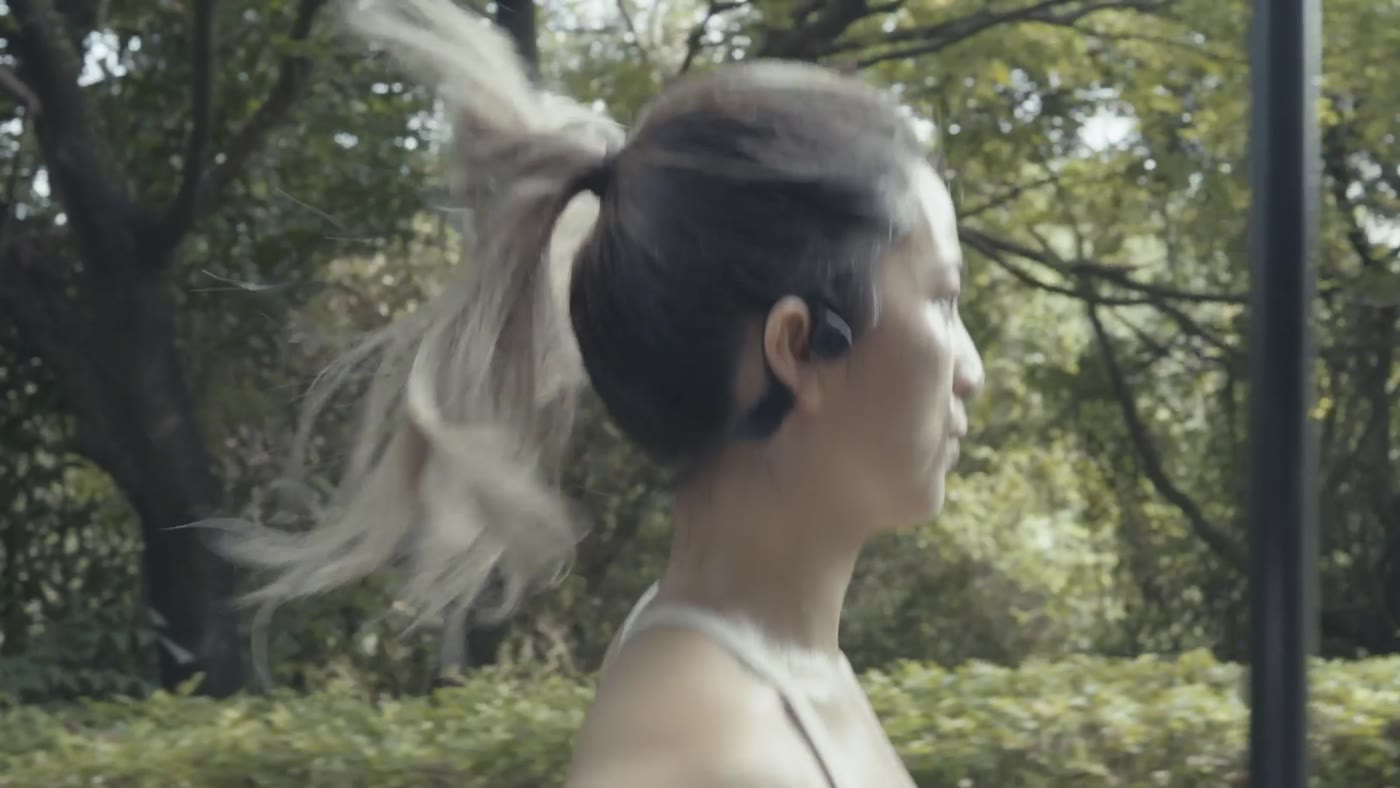 Vrouw hardloopt in het bos met REBØNE open-ear koptelefoon